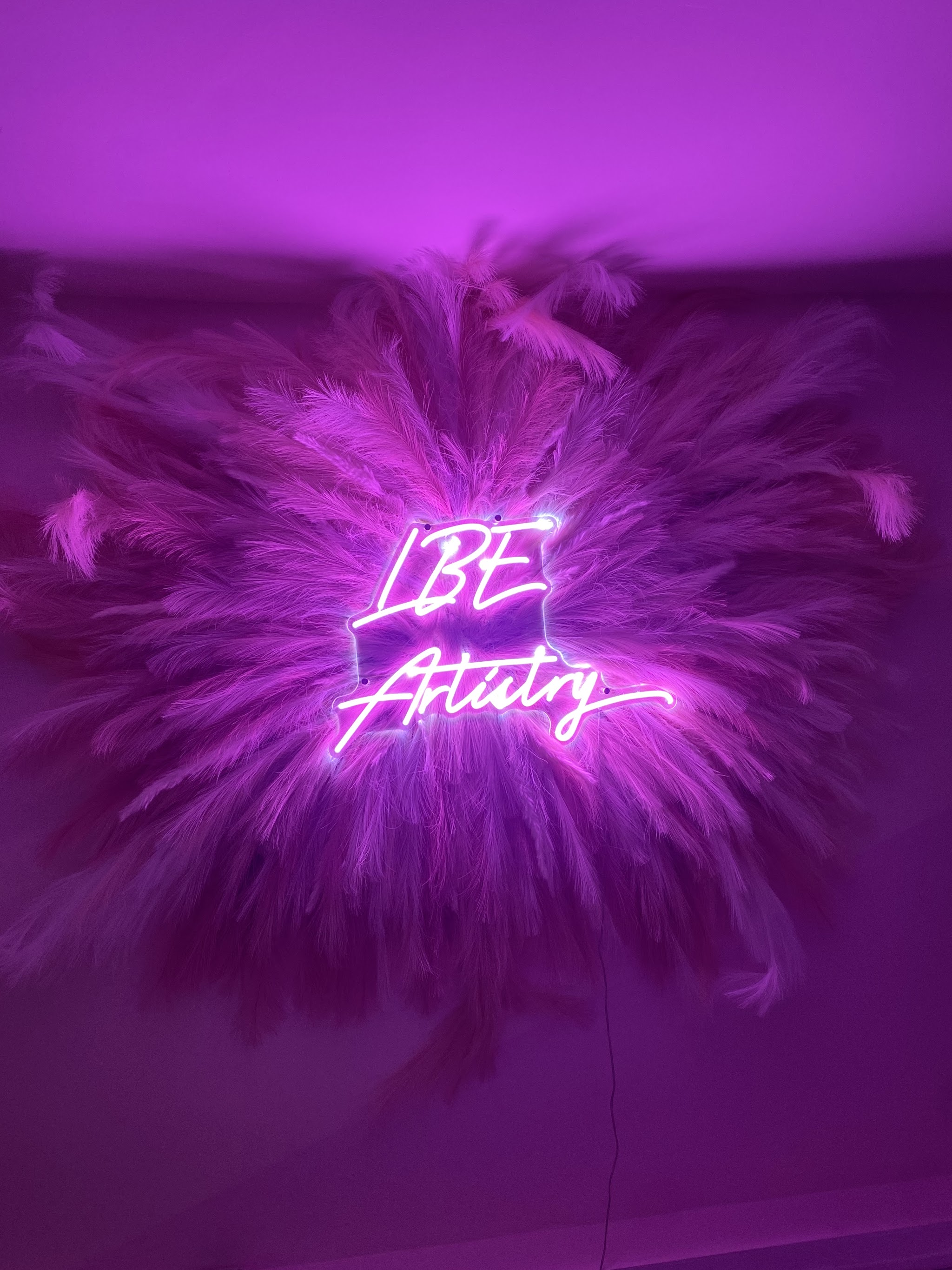 The LBE Artistry neon sign on the purple feather wall
